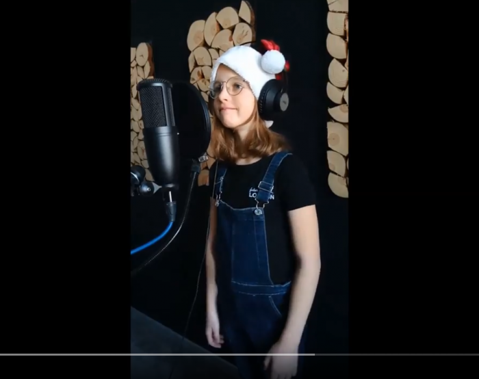 Dziewczynka w mikołajkowej czapce ze słuchawkami na uszach stoi przy mikrofonie